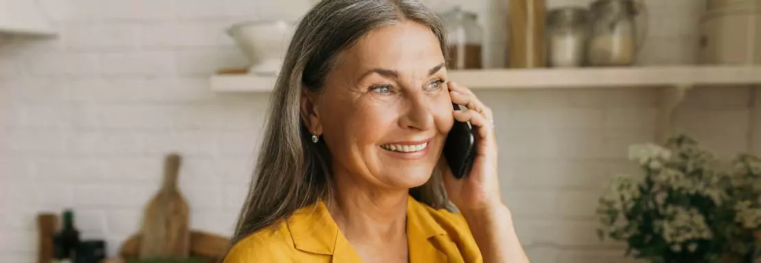 Femme mature parlant joyeusement au téléphone dans sa cuisine