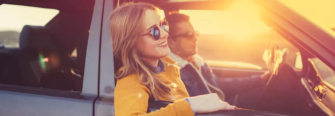 Femme souriante profitant du coucher de soleil en voiture
