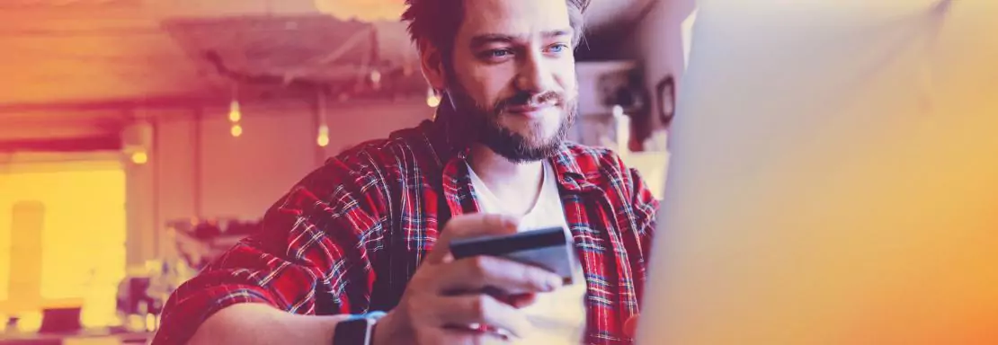Homme souriant utilisant ordinateur et carte bancaire en ligne