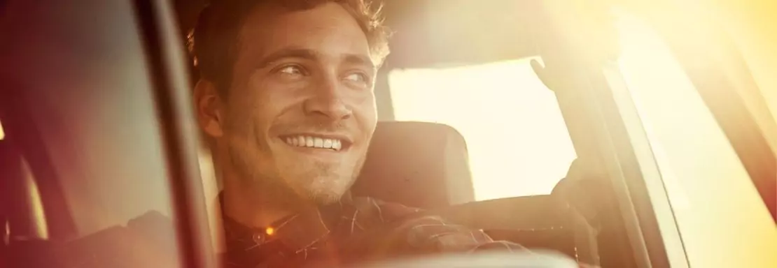 Homme souriant conduisant une voiture au coucher du soleil