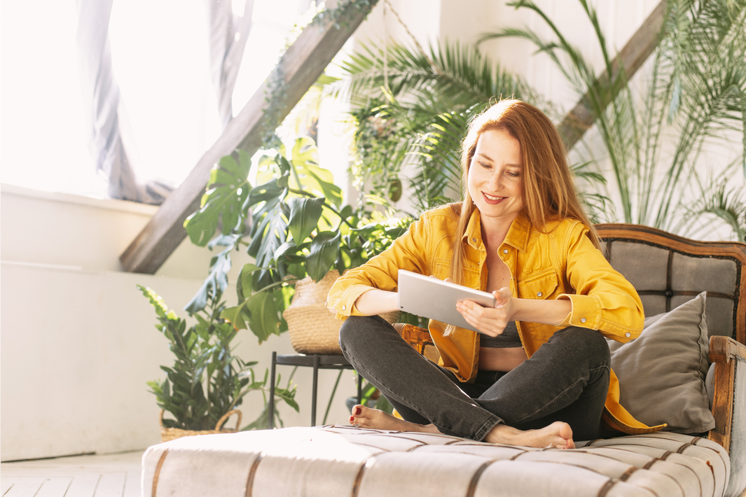 Un femme, assise dans un canapé, regarde une tablette en souriant