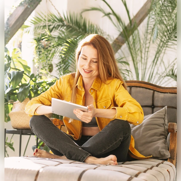 Un femme, assise dans un canapé, regarde une tablette en souriant
