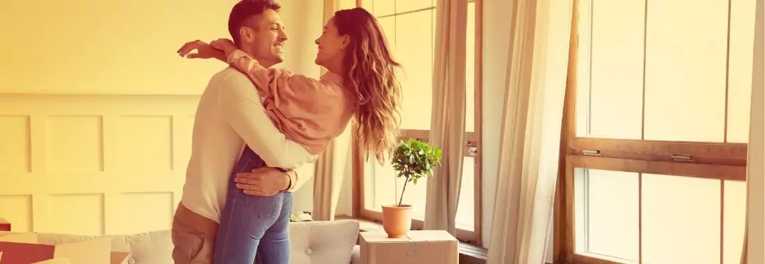 Vrouw en man omhelzen elkaar in een zonnige woonkamer