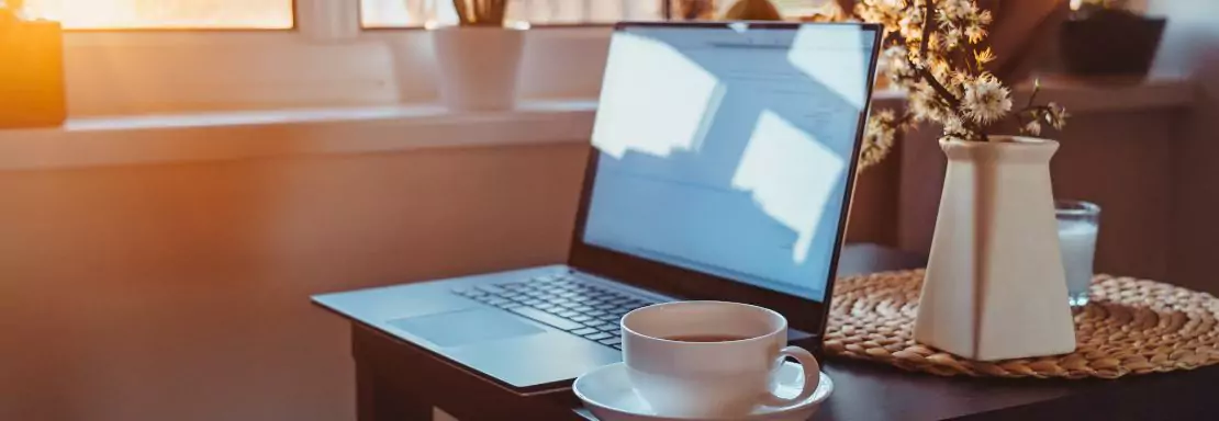 Ontspannen werkplek met laptop, koffie en bloemen in zonlicht