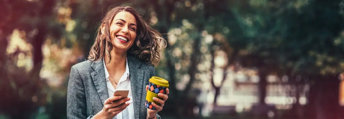 Vrouw met koffiebeker lacht in een natuurlijke omgeving