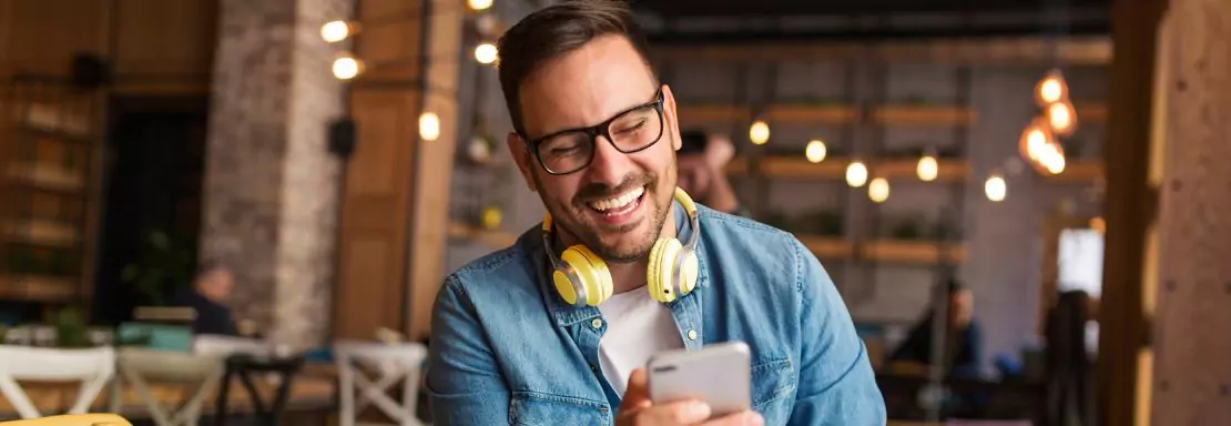 Glimlachende man met telefoon en koptelefoon in café