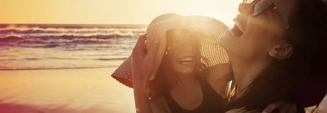Twee vrouwen lachen samen op een zonnig strand