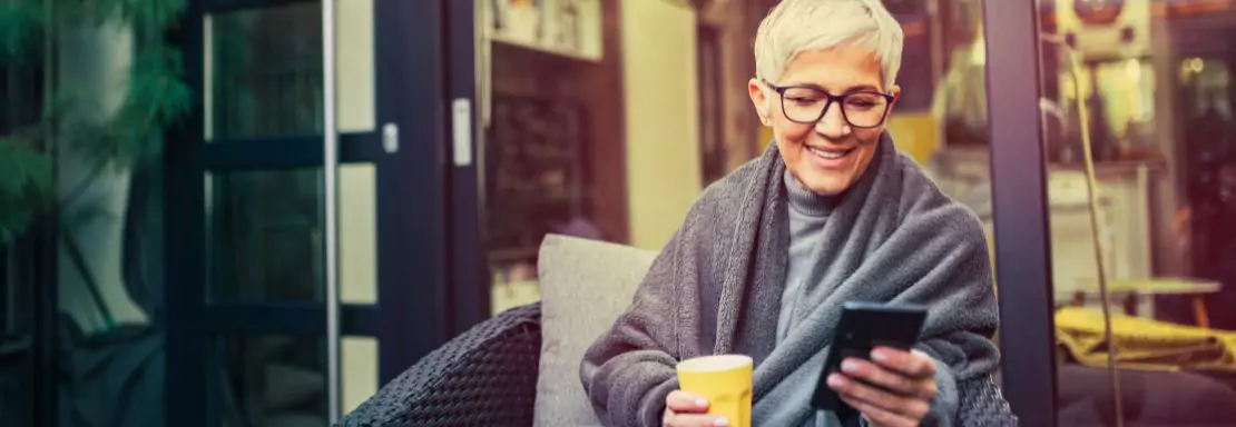 Oudere vrouw kijkt op smartphone op zonnig terras