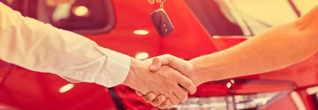 Twee mensen schudden elkaar de hand voor een auto