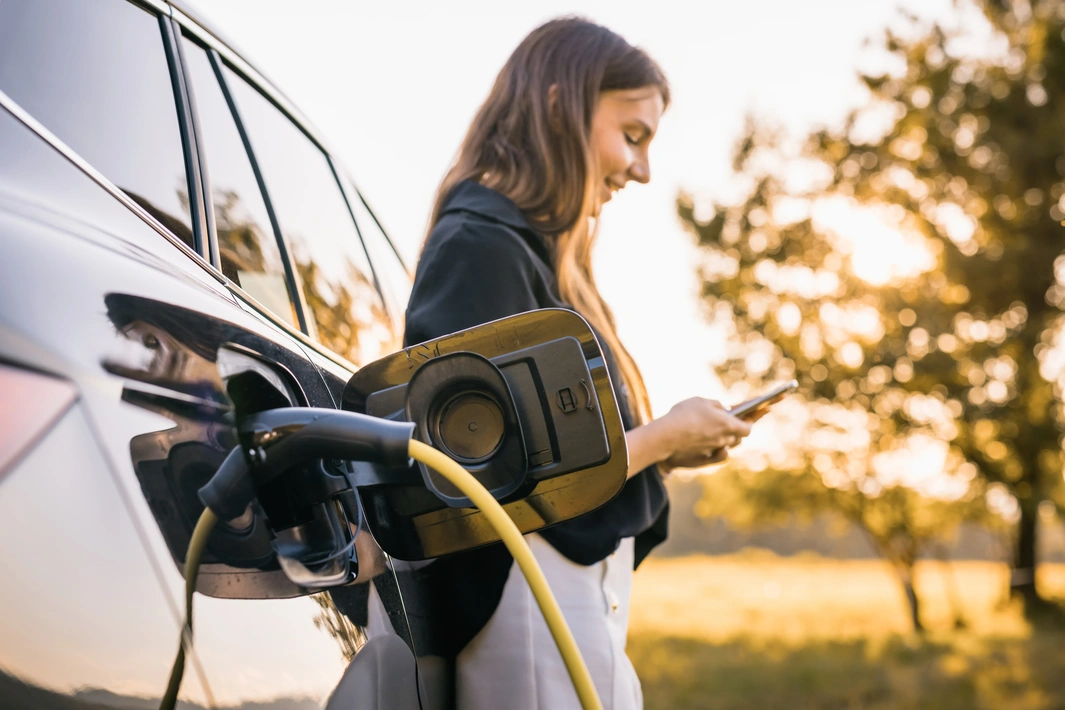 Une femme scrolle sur son smartphone en attendant que sa voiture électrique charge